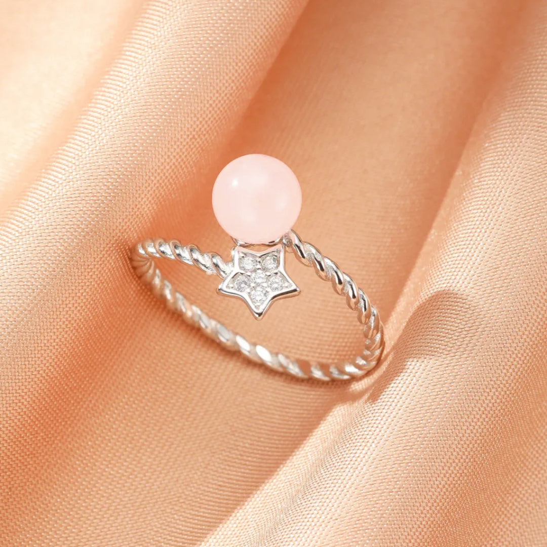 Bague en argent avec une pierre de quartz rose ronde et un pendentif étoile orné de petites pierres scintillantes.