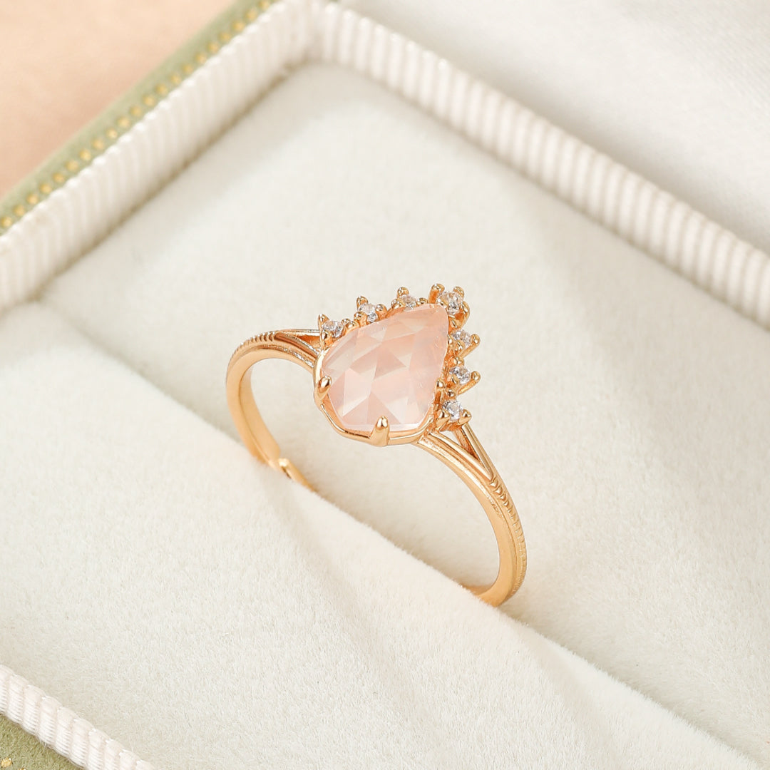 Bague en plaqué or 9K avec une pierre de quartz rose en forme de goutte entourée de petites pierres scintillantes.