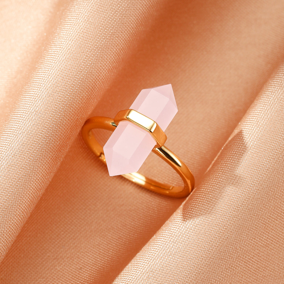Bague fine en argent plaqué or 10K ornée d'un double pointe de quartz rose facetté, posée sur un fond satiné beige.