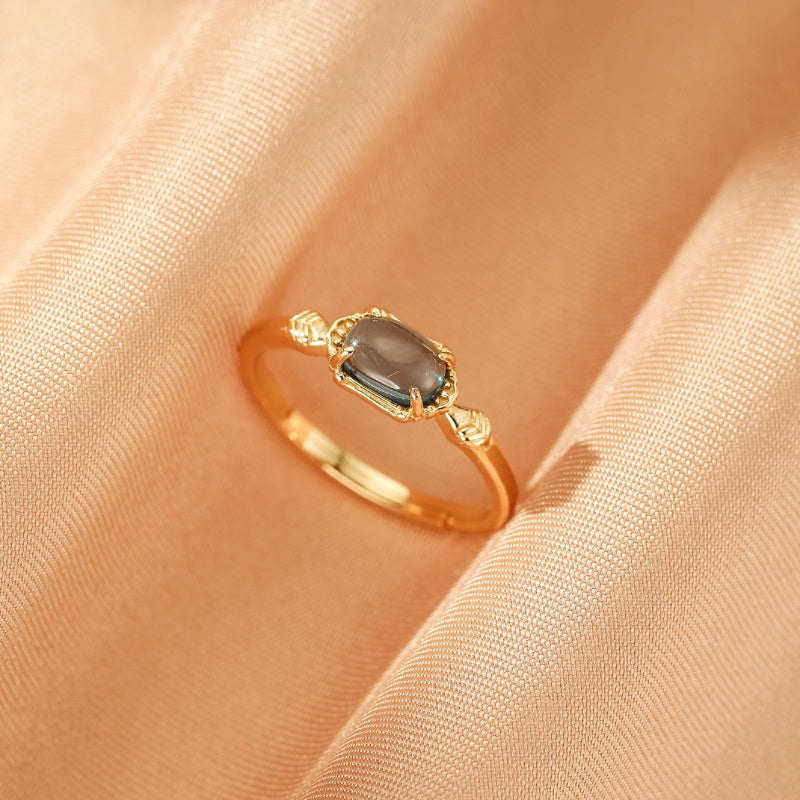 Bague Joie des Cieux en argent plaqué or avec une topaze grise rectangulaire sur un fond de soie pêche.
