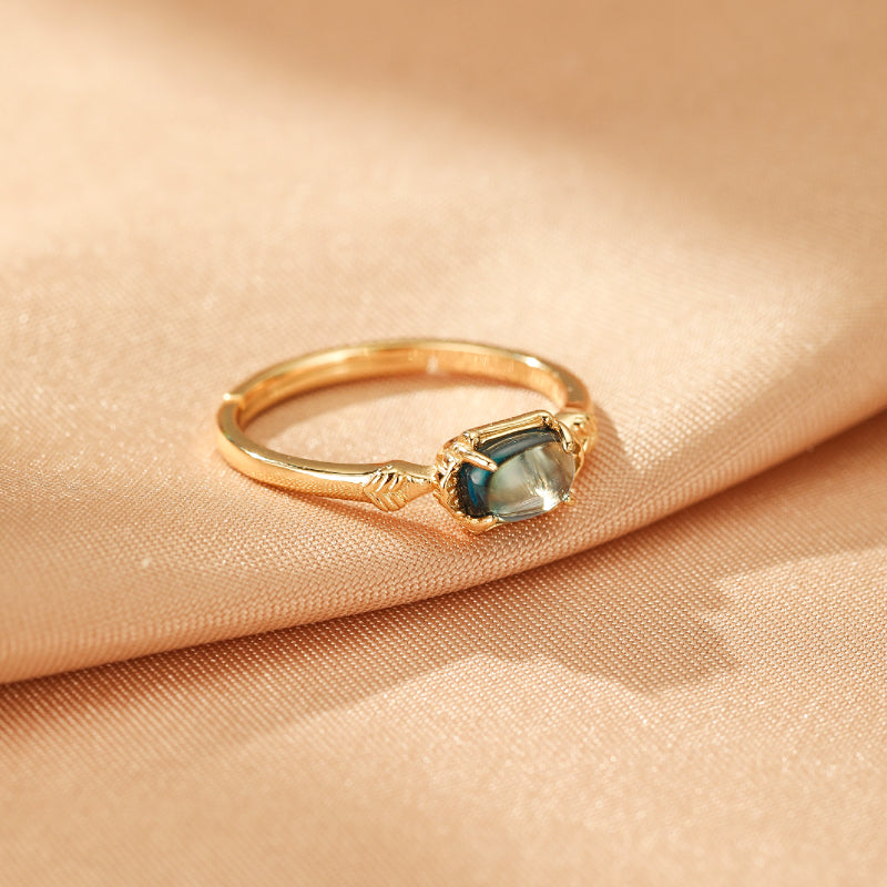 Bague fine en argent plaqué or, ornée d'une topaze bleue rectangulaire aux reflets verts, avec des motifs gravés sur l'anneau.