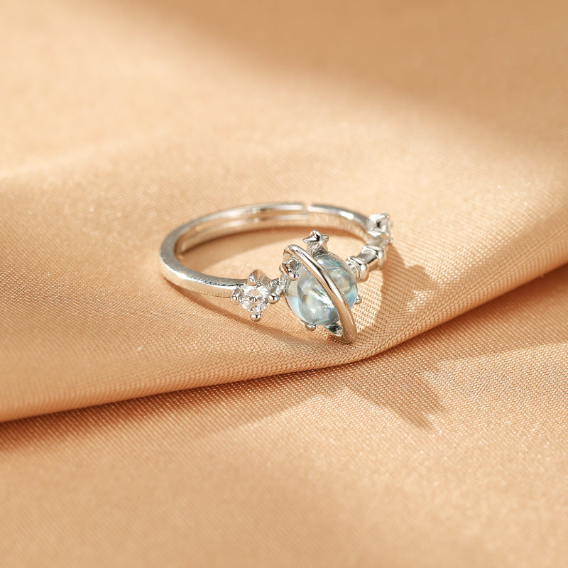 Bague en argent "Univers Enchanté" ornée d'une topaze bleue centrale en forme de planète, entourée d'un anneau et de zirconium.