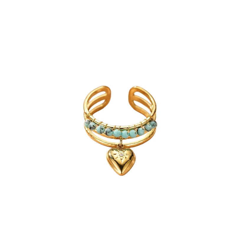 Bague dorée à plusieurs rangs ornée de petites perles turquoise et d'un pendentif en forme de cœur doré avec une petite pierre au centre.