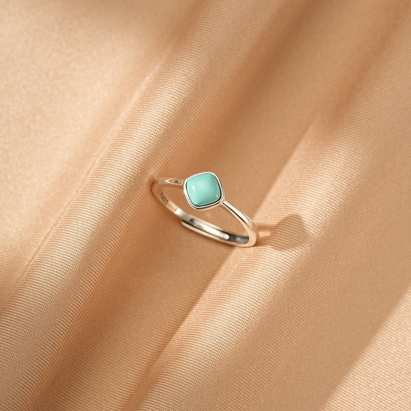 Bague minimaliste en argent 925 avec une petite pierre turquoise carrée de couleur bleu clair, posée sur un tissu satiné couleur champagne.