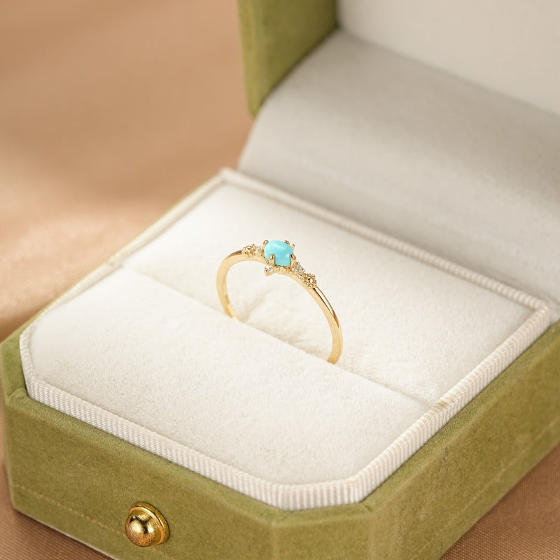 Bague fine en argent plaqué or 14 carats avec une petite turquoise carrée et de minuscules diamants scintillants, présentée dans une boîte à bijoux verte.