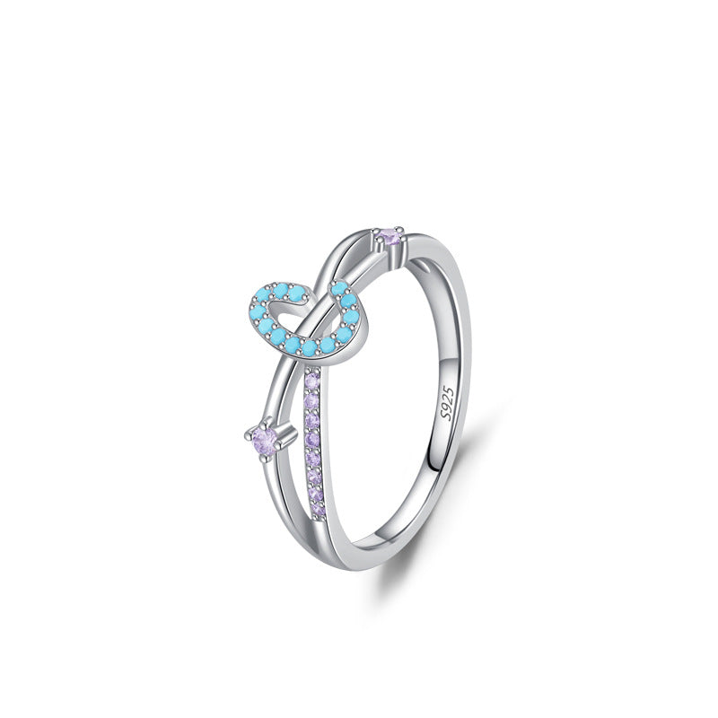 Bague en argent 925 ornée d'un motif en forme de S incrusté de petites pierres turquoise et de zircons violets, avec deux pierres violettes sur l'anneau.
