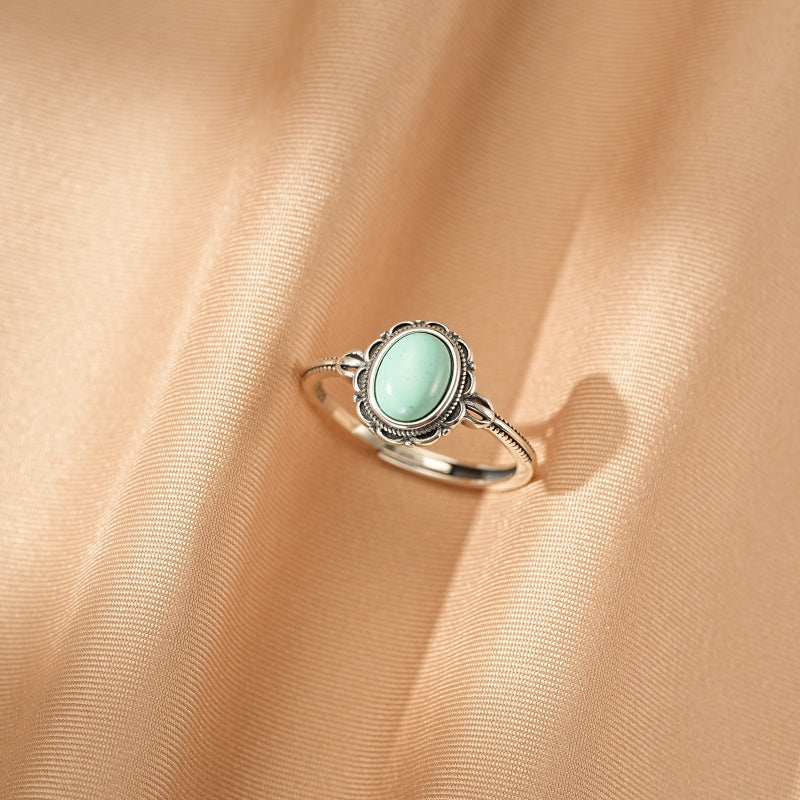 Bague bohème en argent avec une turquoise ovale sertie sur un fond de tissu satiné doré.