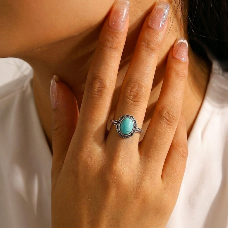 Bague bohème en argent avec une pierre turquoise ovale sertie dans un entourage finement ciselé, portée à l'annulaire.