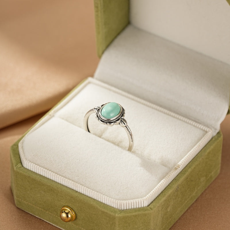 Bague en argent avec une pierre turquoise ovale, style Bohème, présentée dans un écrin vert.