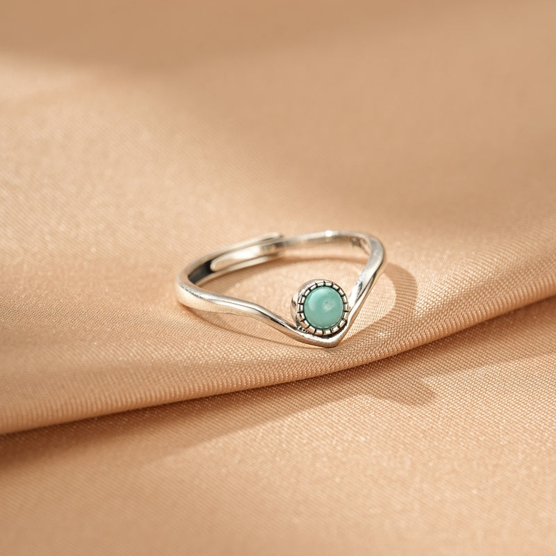 Bague en argent avec une turquoise ronde sertie sur une monture en forme de vague, style bohème, sur fond satiné beige.