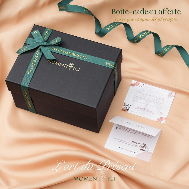 Boîte cadeau noire fermée avec un ruban vert foncé "Vivez du Moment Ici" et un nœud, accompagnée de deux cartes illustrées sur un fond satiné pêche. @shared #shared