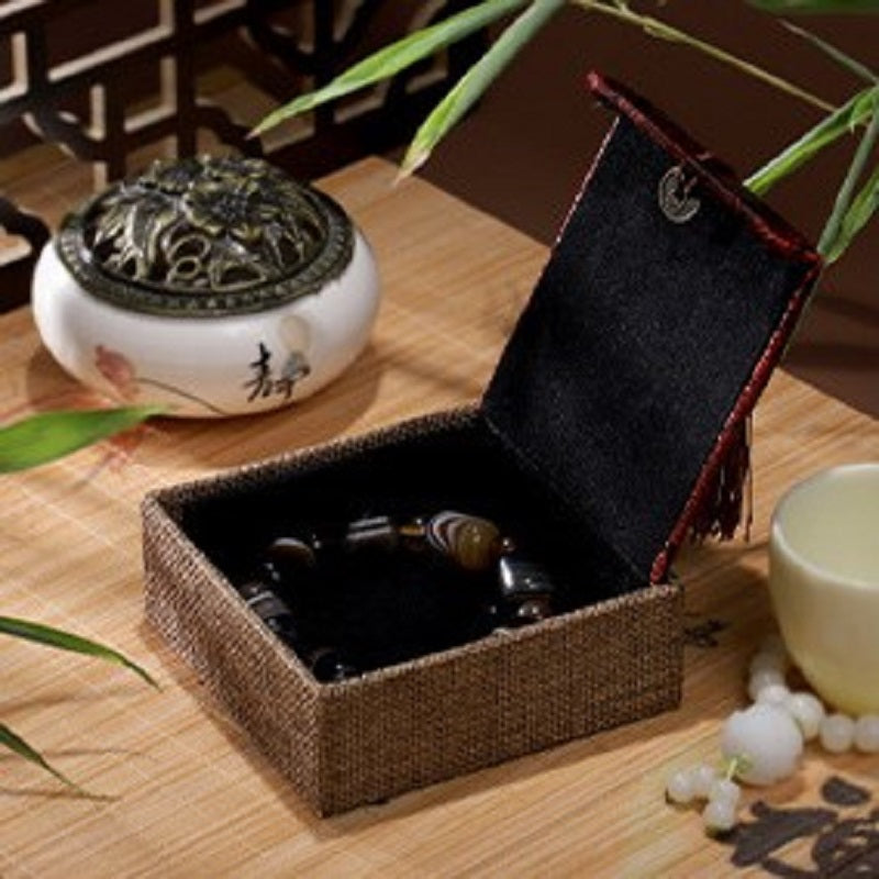 Boîte cadeau zen en lin avec un bracelet en pierres naturelles à l'intérieur, posée sur un plateau en bois à côté d'un brûle-parfum.