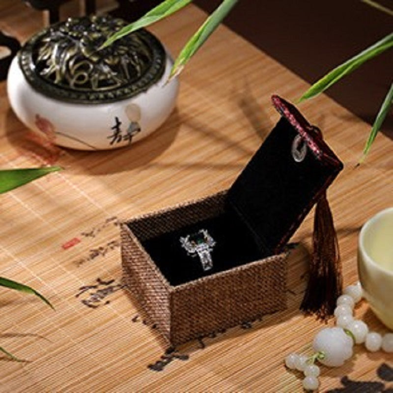 Boîte cadeau zen en lin brun avec un anneau incrusté de pierres vertes à l'intérieur, sur un tapis en bambou.