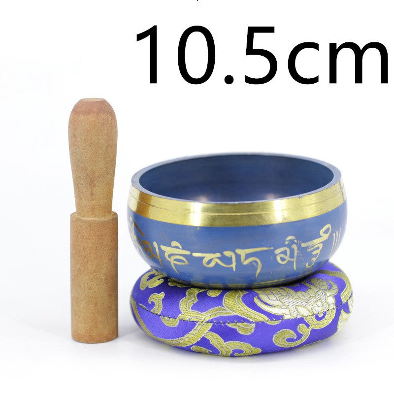 Bol chantant tibétain bleu de 10.5 cm, orné de mantras dorés, posé sur un coussin violet brodé d'un dragon.