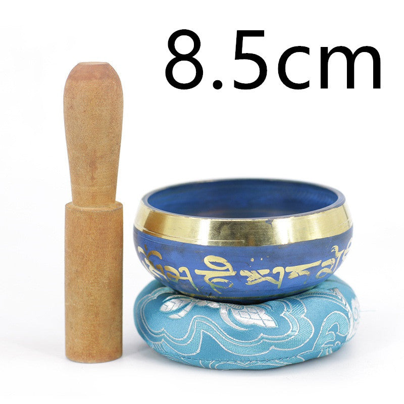 Bol chantant tibétain bleu de 8,5 cm avec des mantras dorés, monté sur un coussin bleu orné, et un maillet en bois à côté.