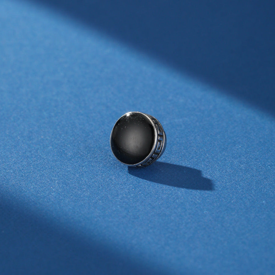 Boucle d'oreille homme en argent avec un disque noir central et une gravure de motif grec sur le pourtour.