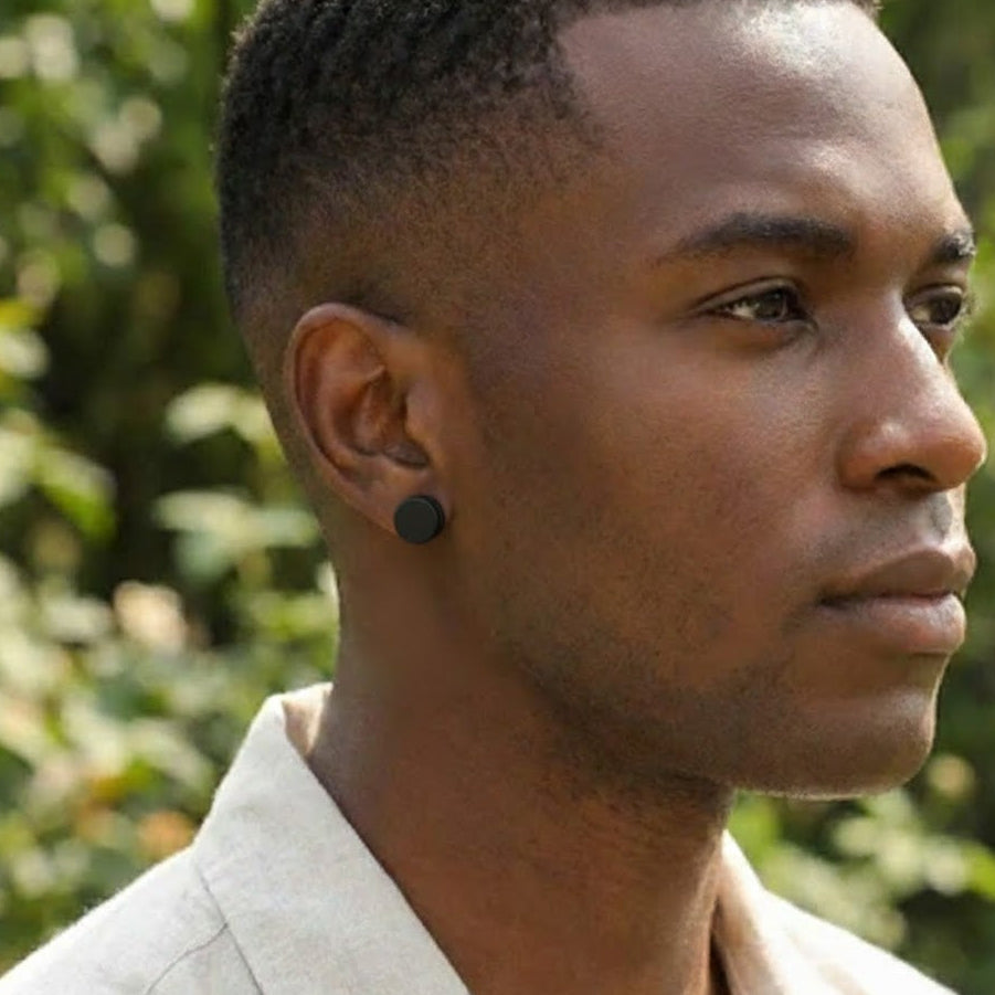 Boucle d'oreille homme cercle noir, discret et moderne, portée par un homme sur fond végétal flou.