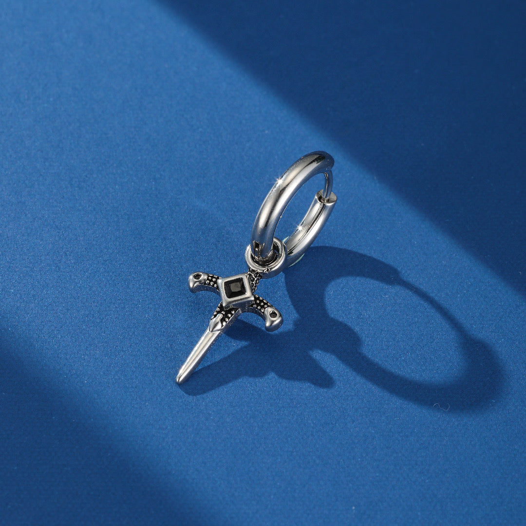 Boucle d'oreille homme style Viking avec un pendentif en forme d'épée argentée ornée d'une pierre noire centrale carrée, sur fond bleu.