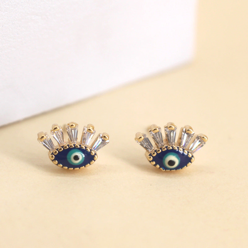 Paire de boucles d'oreilles en forme d'œil bleu stylisé avec des cristaux blancs et une monture dorée, style mauvais œil.