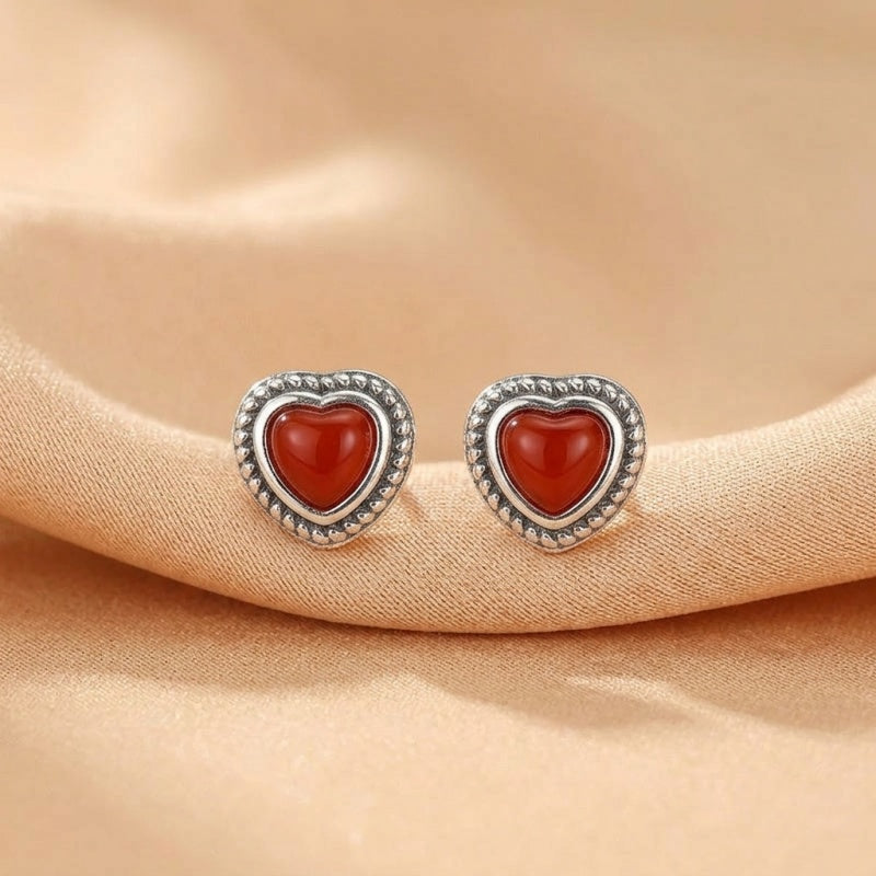 Boucles d'oreilles en argent ornées d'une pierre d'agate rouge en forme de cœur, avec un contour finement détaillé de petites perles argentées.