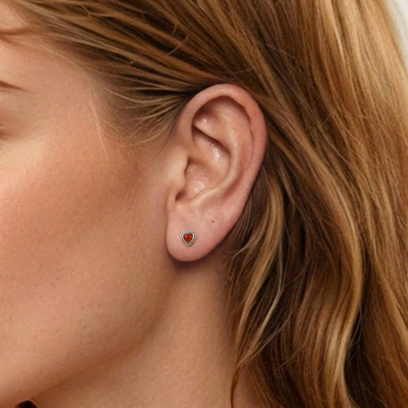 Boucle d'oreille en argent avec une petite pierre d'agate rouge en forme de cœur, portée par une femme.