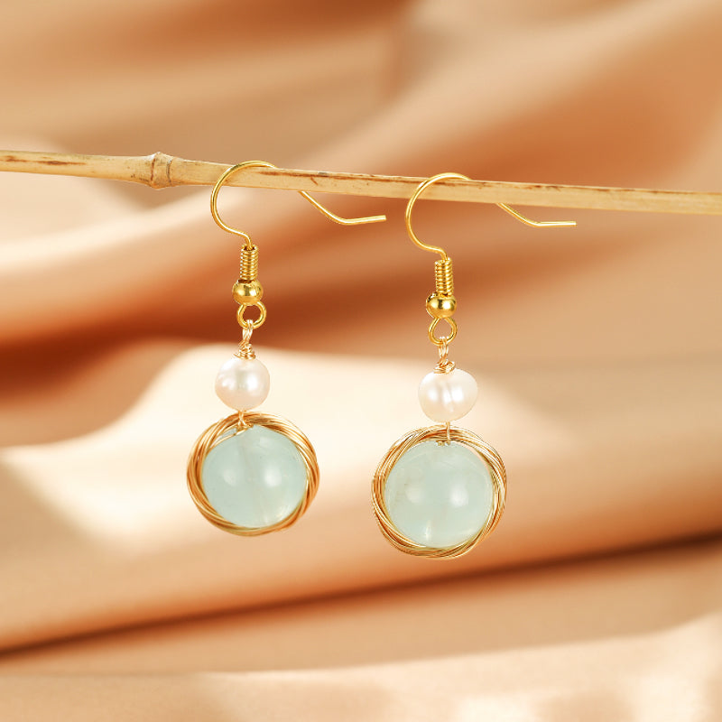 Paire de boucles d'oreilles pendantes "Pure Harmonie" ornées d'une aigue-marine ronde et d'une perle blanche, suspendues à des crochets dorés.