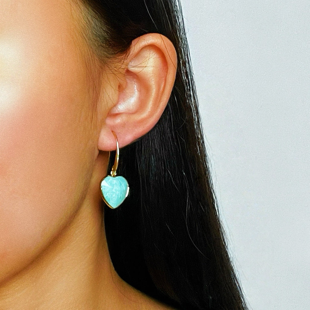 Boucle d'oreille en forme de cœur en amazonite bleue et lapis-lazuli avec une monture dorée, portée à l'oreille gauche d'une femme.