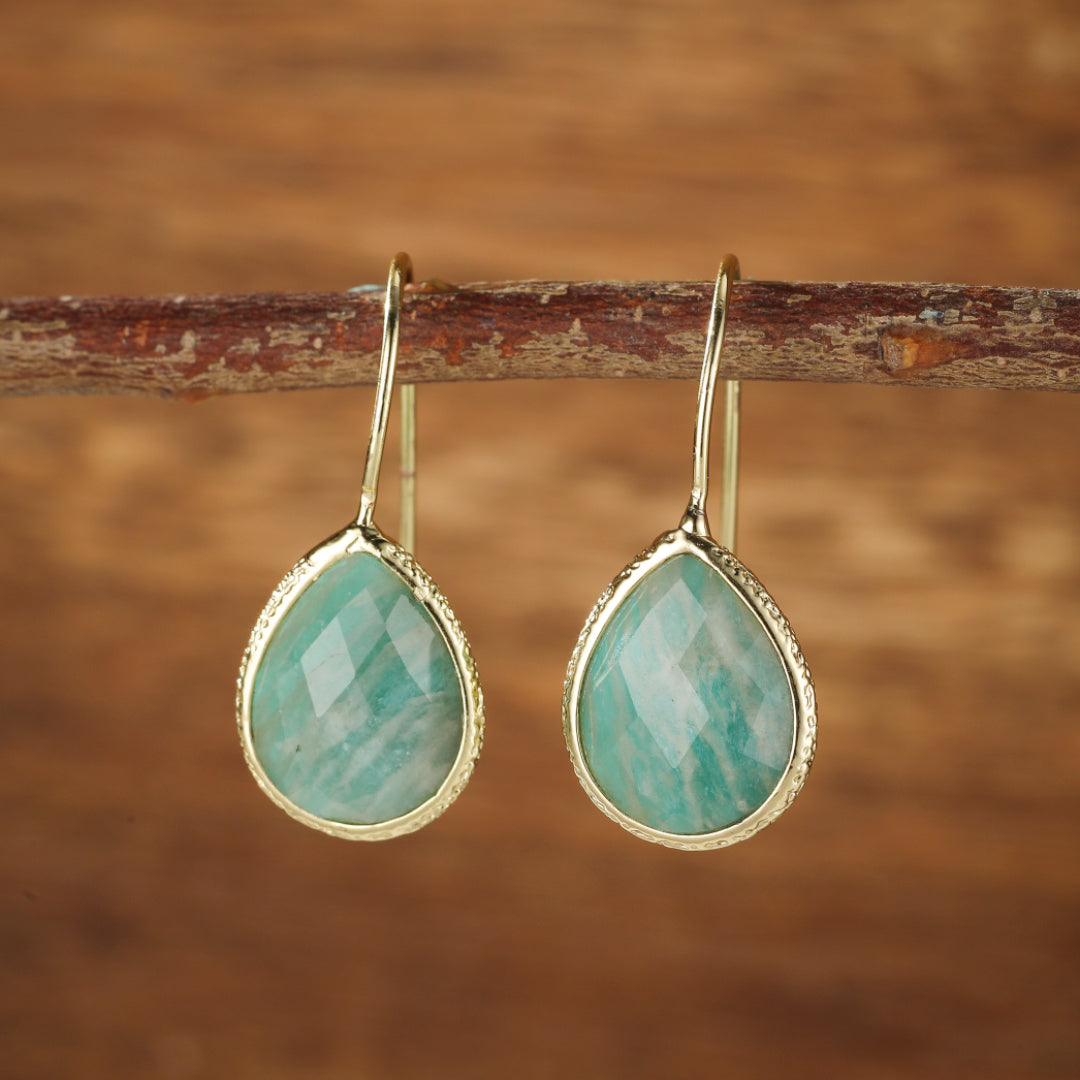 Boucles d'oreilles pendantes en amazonite verte en forme de goutte, serties dans un cadre doré texturé, suspendues à une branche.