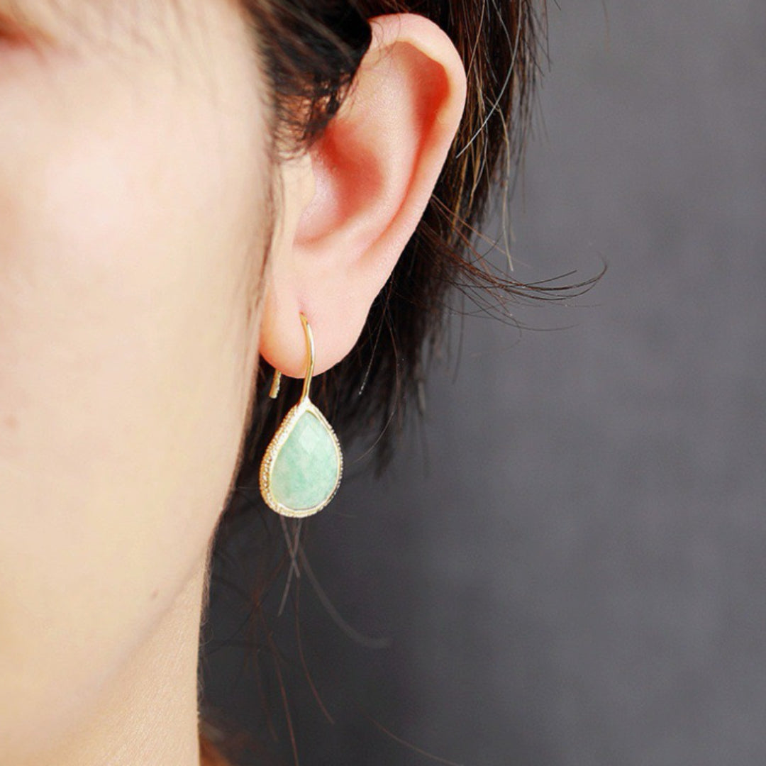 Boucle d'oreille pendant en forme de goutte avec une pierre d'amazonite verte et un contour doré, portée à l'oreille d'une femme.