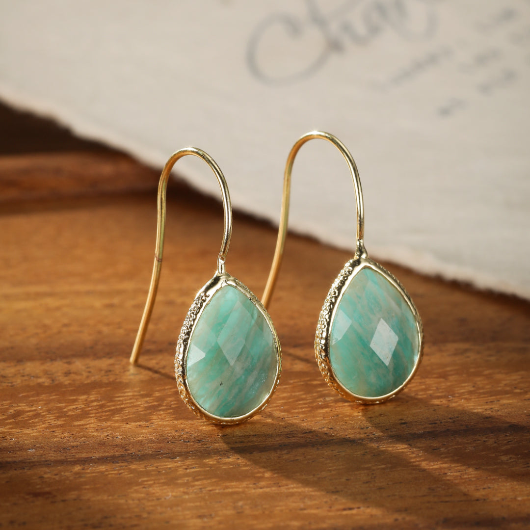 Boucles d'oreilles pendantes en amazonite facettée et or, forme goutte d'eau, sur fond en bois