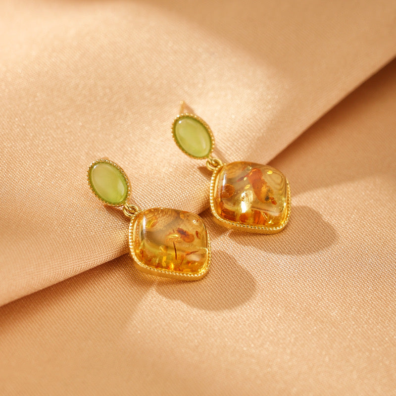 Boucles d'oreilles pendantes en ambre et pierre verte type jade, montées sur argent plaqué or, design élégant et lumineux sur fond satiné beige