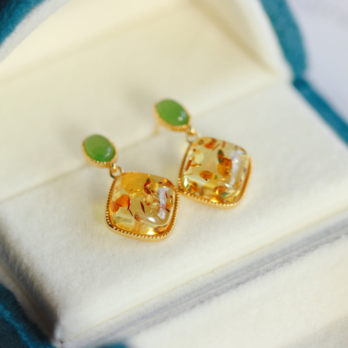 Boucles d'oreilles élégantes en ambre naturel et jade vert, montées sur argent plaqué or, présentées dans un écrin bleu.