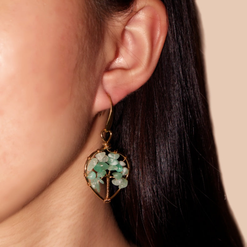 Boucles d'oreilles en forme d'arbre céleste avec des pierres d'améthyste et un fil de cuivre doré, portées à l'oreille d'une femme.