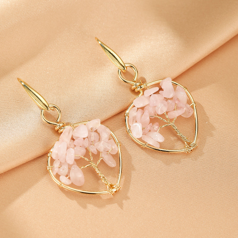 Boucles d'oreilles en forme d'arbre céleste avec des pierres d'améthyste rose et des fils de cuivre dorés sur un fond de soie beige.