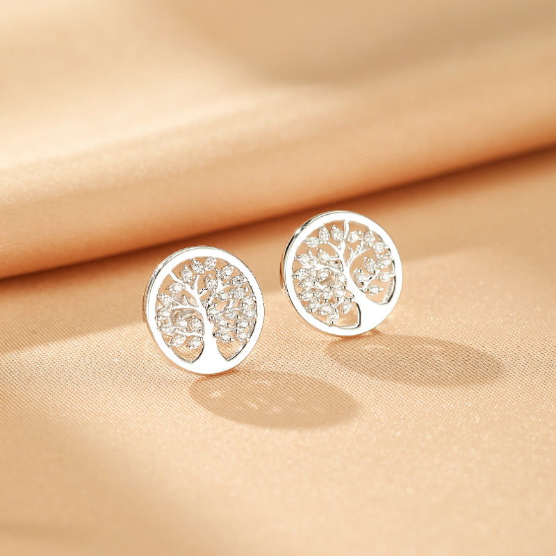 Paire de boucles d'oreilles Arbre de Vie en argent S925, ornées de petites pierres scintillantes, sur un fond satiné couleur pêche.