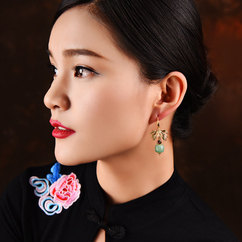 Boucles d'oreilles plaqué or ornées d'une feuille dorée et d'une perle d'aventurine verte, portées par une femme au profil.