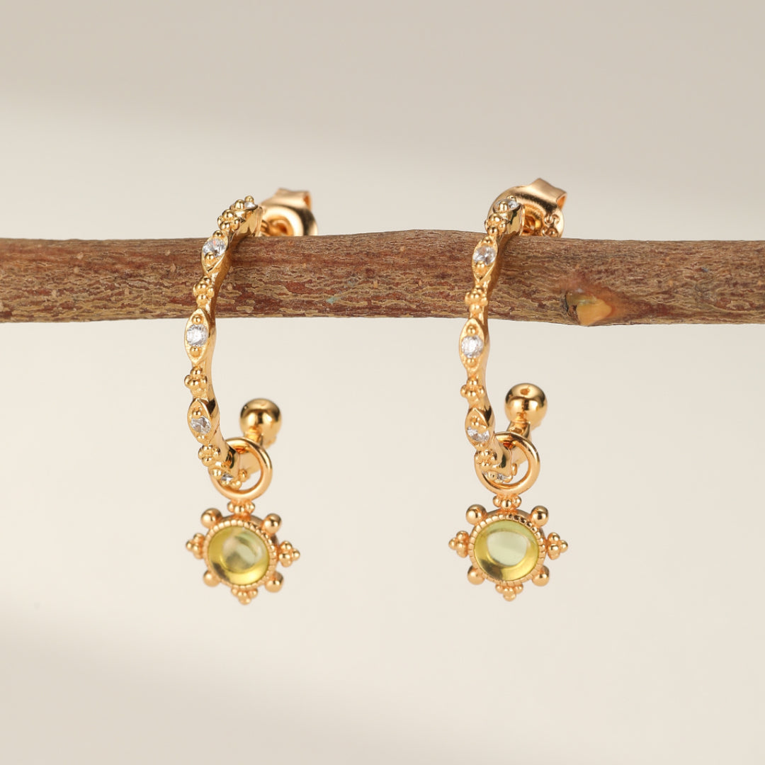 Paire de boucles d'oreilles créoles en argent plaqué or, ornées de péridots et de petites pierres d'oxydes de zirconium, suspendues à une branche.