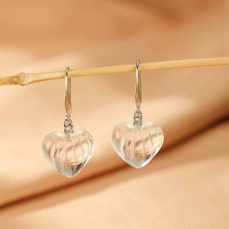 Boucles d'oreilles en forme de cœur en cristal de roche transparent avec des détails texturés, suspendues à des crochets en argent.