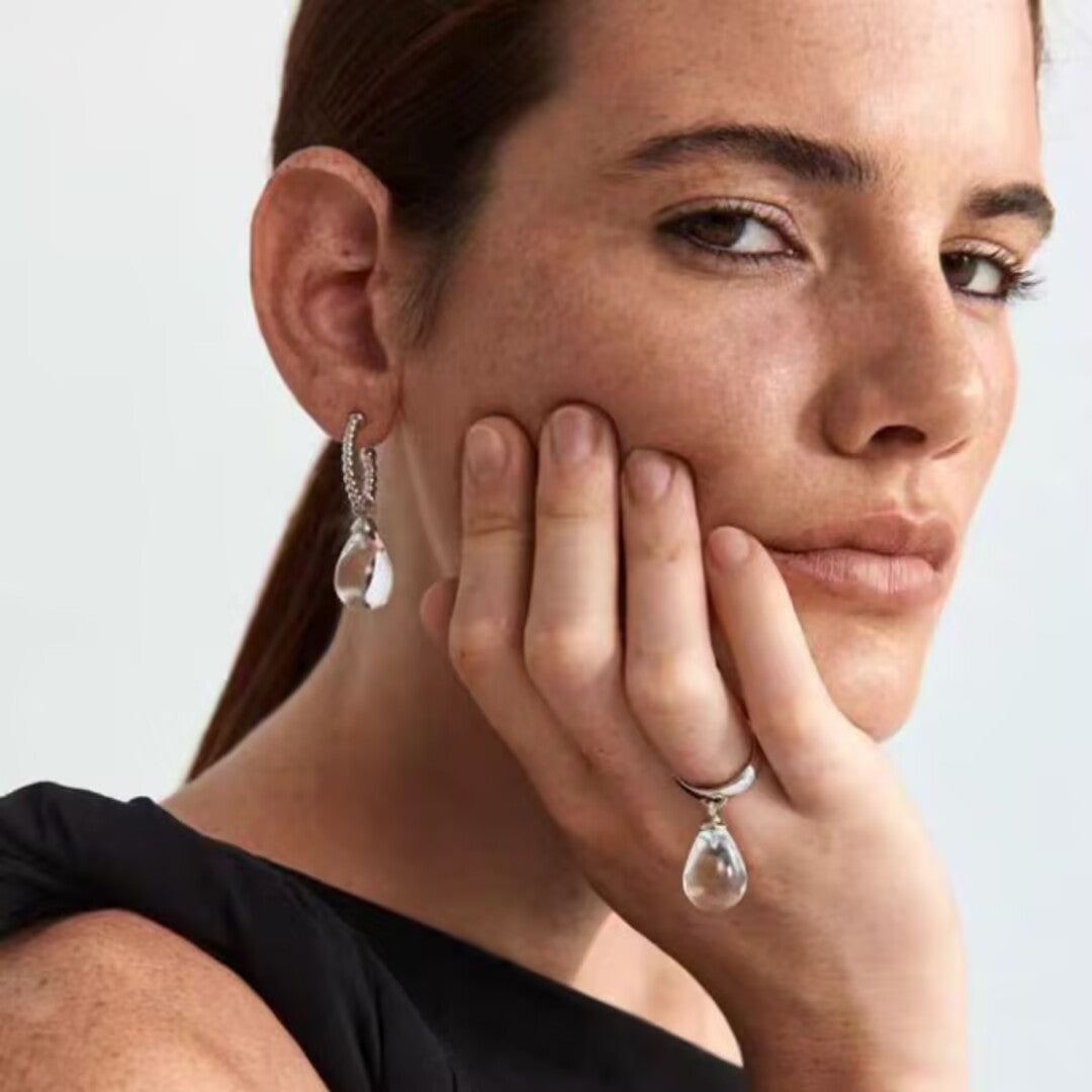 Gros plan sur une femme portant des boucles d'oreilles en cristal de roche en forme de goutte et une bague assortie en argent.