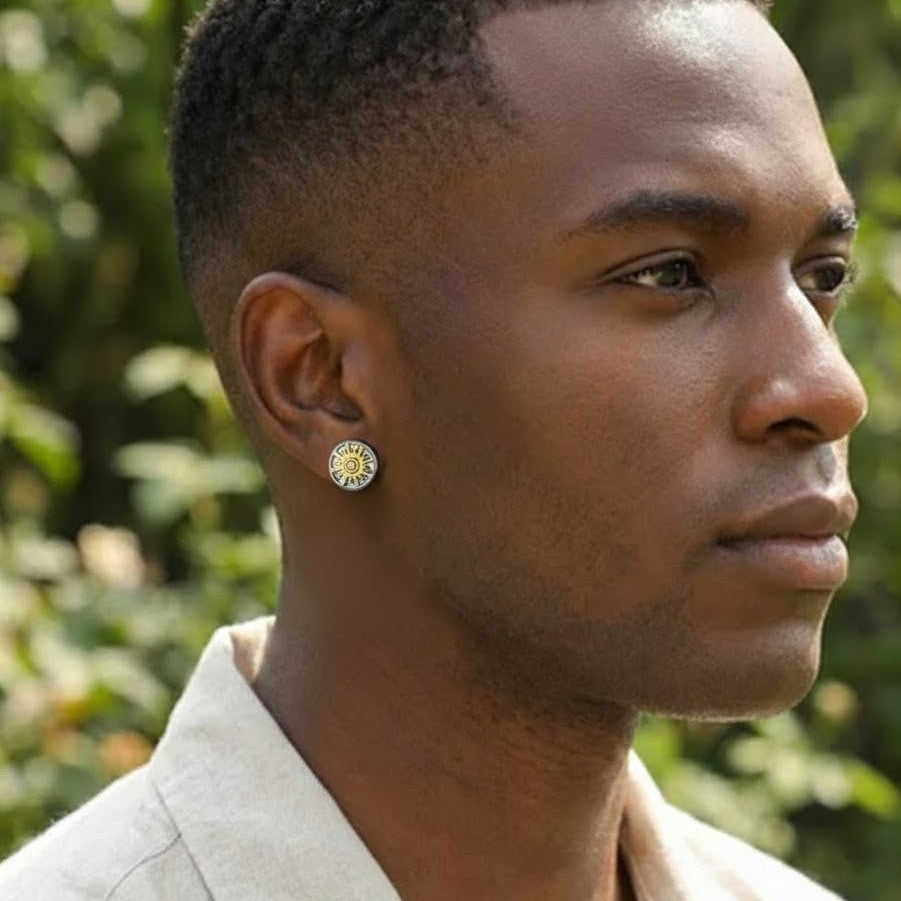Boucle d'oreille homme "Duo Cosmique" de couleur argentée et dorée avec un motif solaire stylisé, portée par un homme sur fond de verdure.