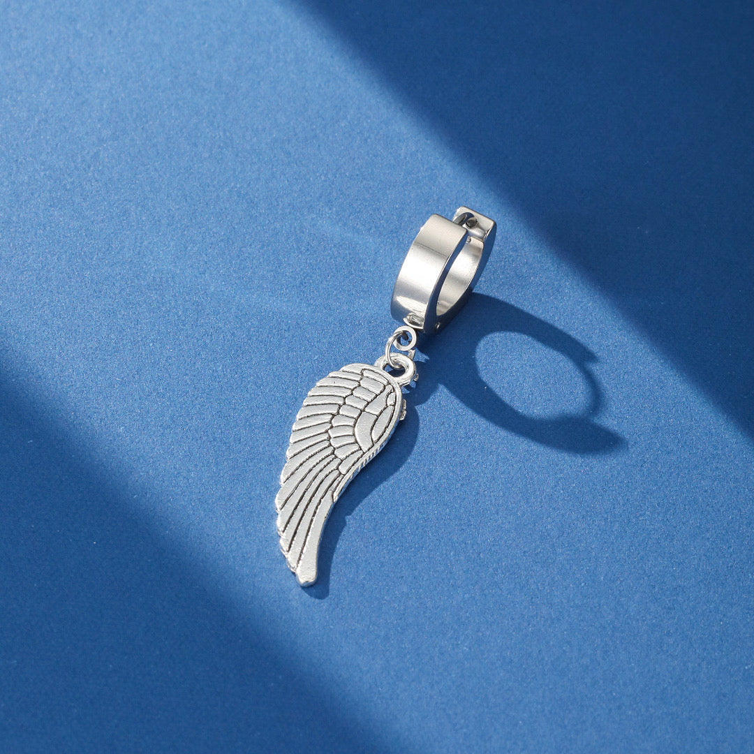 Boucle d'oreille homme style rebelle avec un pendentif aile d'ange argentée détaillée sur fond bleu.