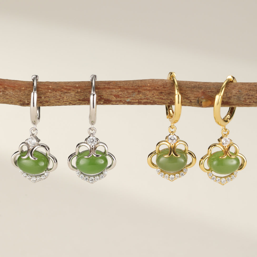 Paire de boucles d'oreilles pendantes en argent et en or avec des pierres de jade verte ovale et des accents de zircon cubique, suspendues à une branche.