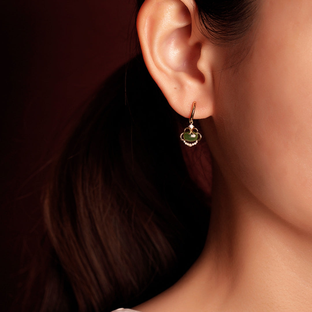 Boucle d'oreille plaquée or avec un pendentif en forme de trèfle orné d'une pierre de jade verte et de petites pierres blanches scintillantes, portée à l'oreille d'une femme.