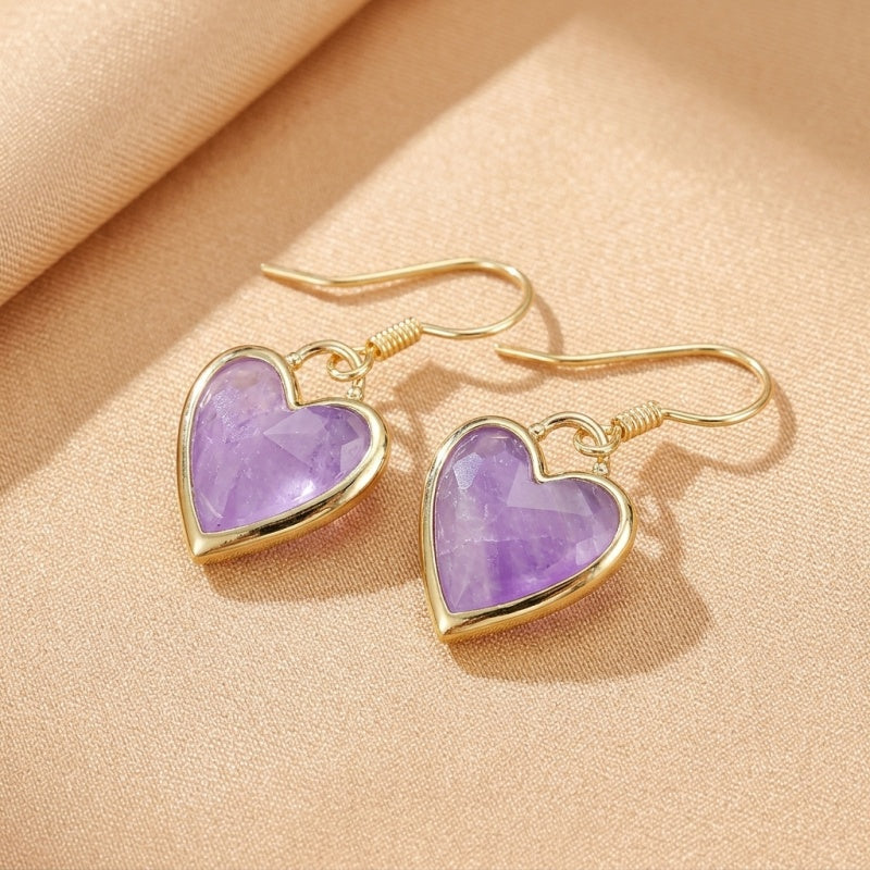Boucles d'oreilles cœur en labradorite violette avec monture dorée, sur un fond texturé beige.