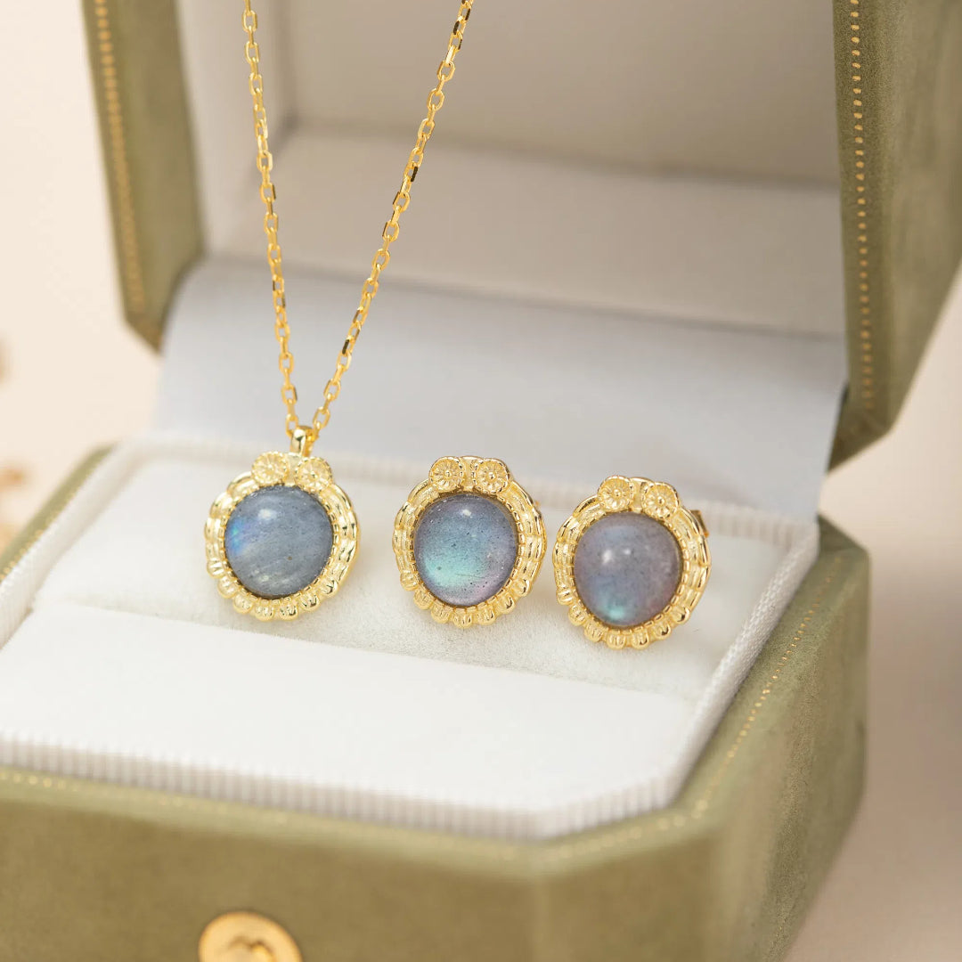 Ensemble de boucles d'oreilles et pendentif en labradorite avec monture travaillée en argent plaqué or, présenté dans un écrin vert.