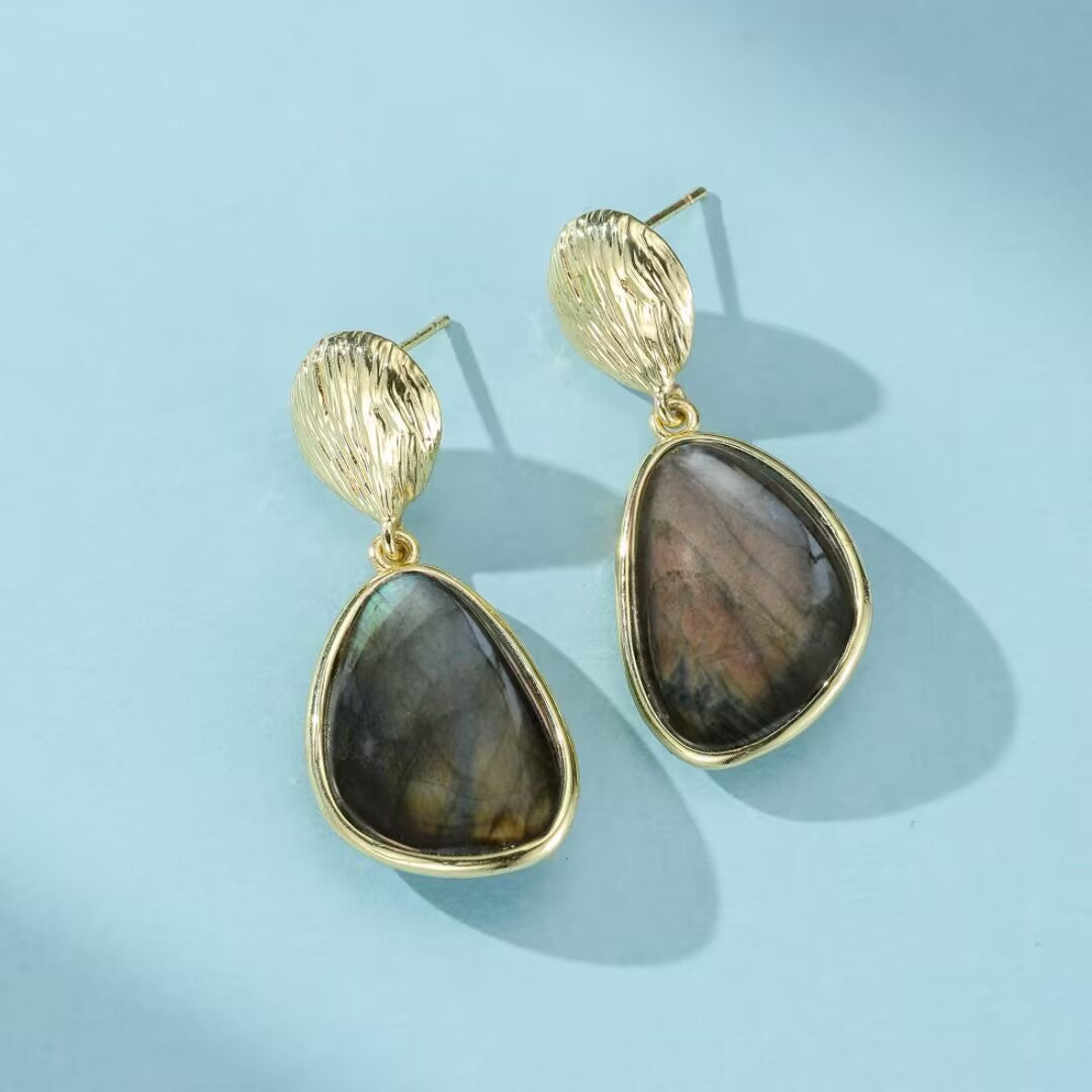 Paire de boucles d'oreilles pendantes en labradorite aux reflets bleutés et cuivrés, serties dans un contour doré, avec une finition texturée sur la partie supérieure.