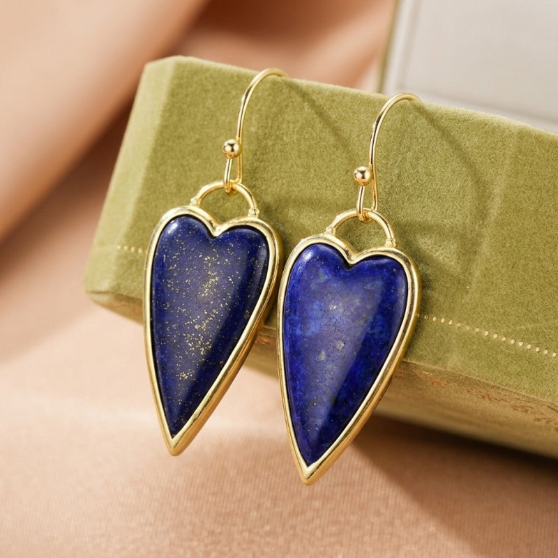 Boucles d'oreilles en forme de cœur en lapis-lazuli avec monture dorée, présentées sur un écrin vert.