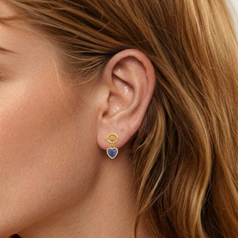 Boucle d'oreille dorée en forme de cœur avec pierre bleue lapis-lazuli, portée à l'oreille d'une femme.