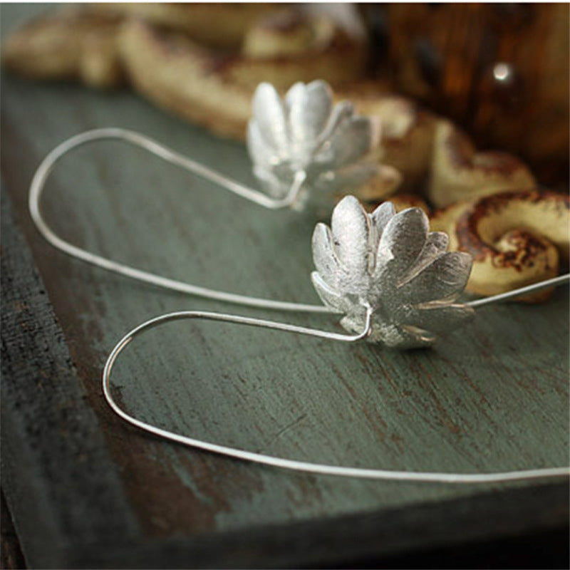 Boucles d’oreilles en argent en forme de lotus avec un design inspiré de la nature, reposant sur une surface en bois patiné.