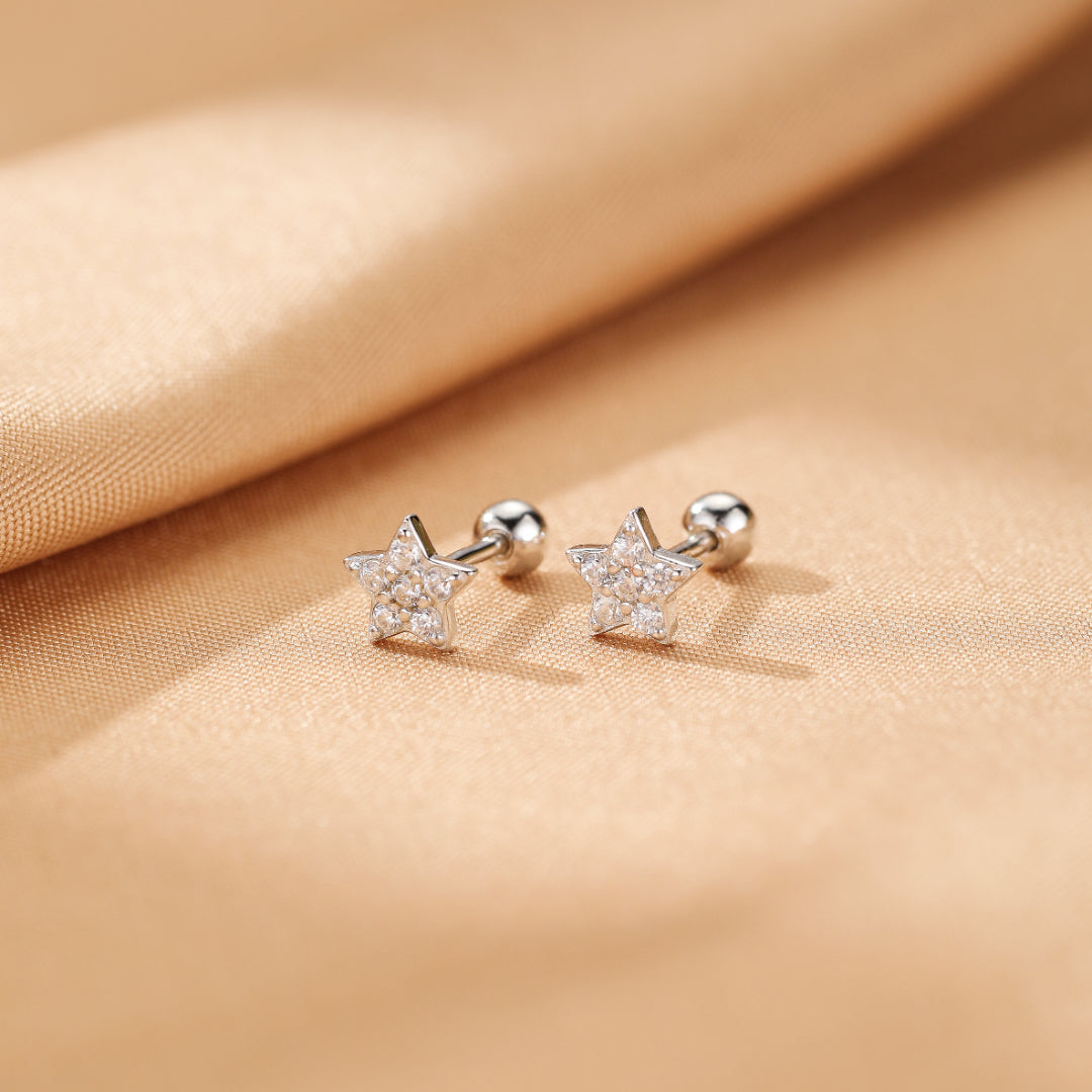 Paired sterling silver star-shaped earrings adorned with tiny cubic zirconia stones, resting on a satin fabric.